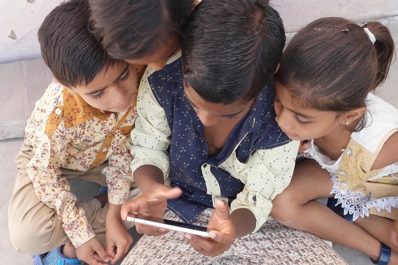 Children huddle together while one plays with a mobile phone
