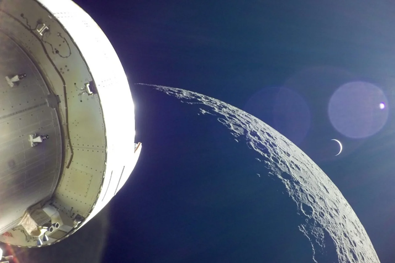 A spacecraft views the Moon and a crescent Earth in space.