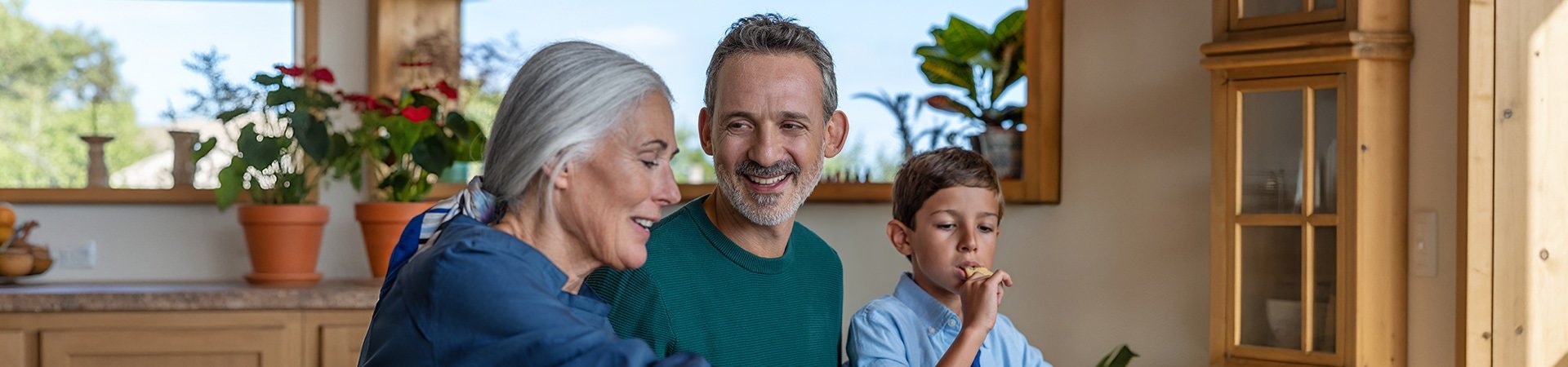 Ein lächelnder Mann und eine ältere Frau sehen einem kleinen Jungen zu, der in der Küche isst.
