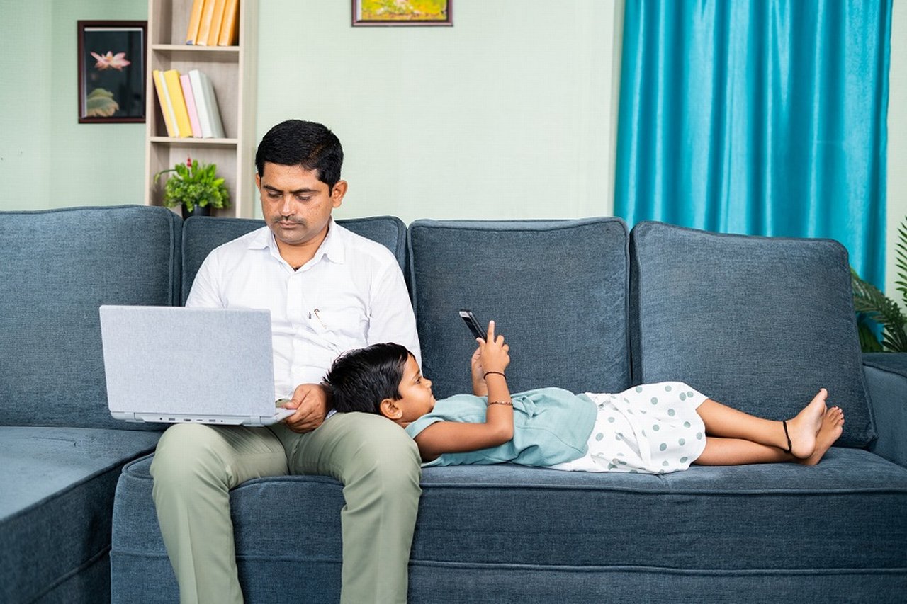 Father works on laptop while son plays with cell phone