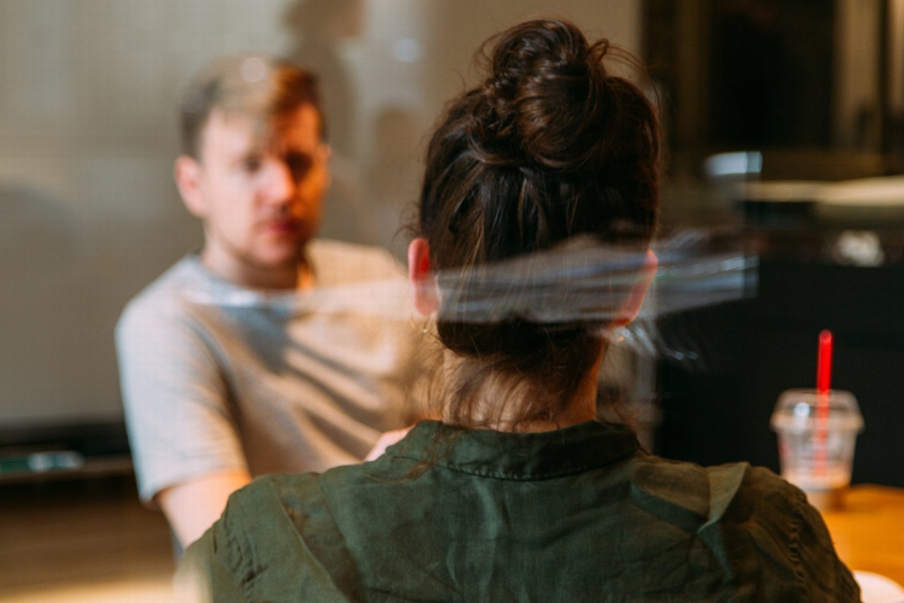 The photo shows a man and a woman sitting at a table having coffee and talking.
