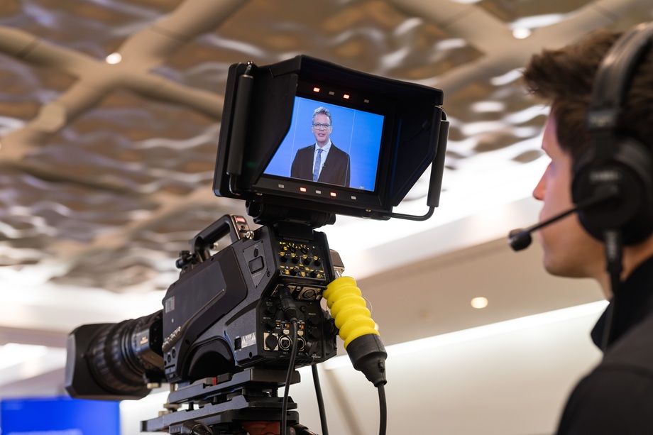 A cameraman operating a professional broadcast camera with a view of Christian Sewing on the monitor.